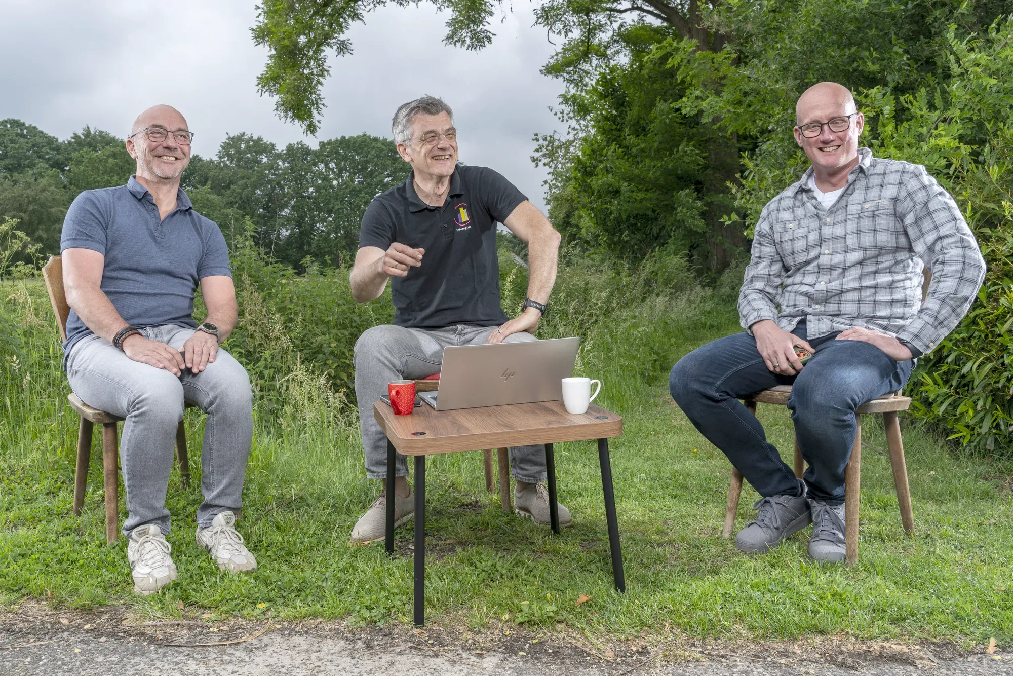 Drie collega’s van InfoReports in gesprek rond een laptop, buiten