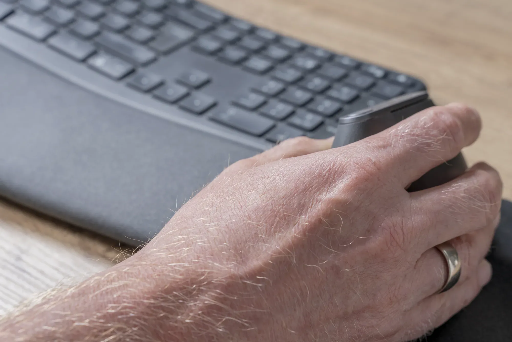 Hand op een muis naast een toetsenbord op een bureau